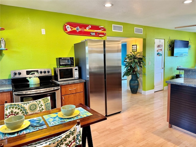 kitchen with appliances with stainless steel finishes, visible vents, brown cabinetry, and light wood-style flooring