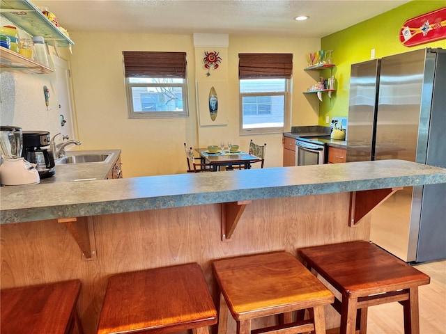 kitchen with a sink, stainless steel appliances, open shelves, and a kitchen breakfast bar