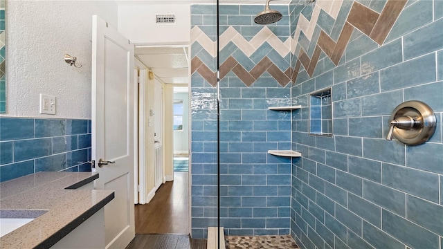 full bathroom with visible vents, wood finished floors, a tile shower, and a textured wall