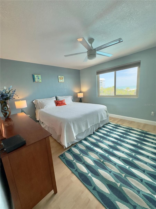 bedroom featuring baseboards, light wood finished floors, ceiling fan, and a textured ceiling