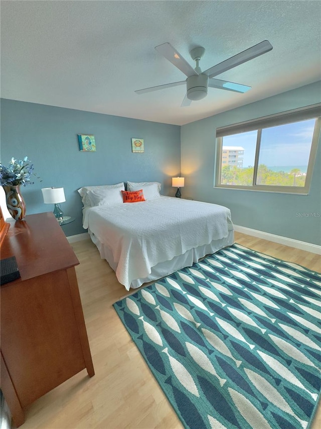 bedroom with a textured ceiling, baseboards, light wood-type flooring, and a ceiling fan