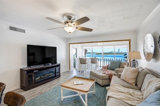 living area featuring wood finished floors, crown molding, ceiling fan, a fireplace, and baseboards