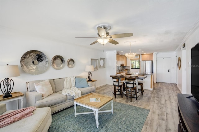living room featuring ceiling fan, light wood-style flooring, baseboards, crown molding, and a chandelier