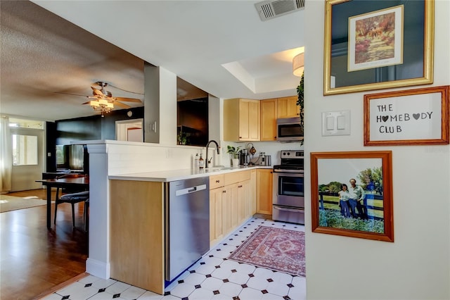 kitchen featuring appliances with stainless steel finishes, a sink, light brown cabinets, and light flooring