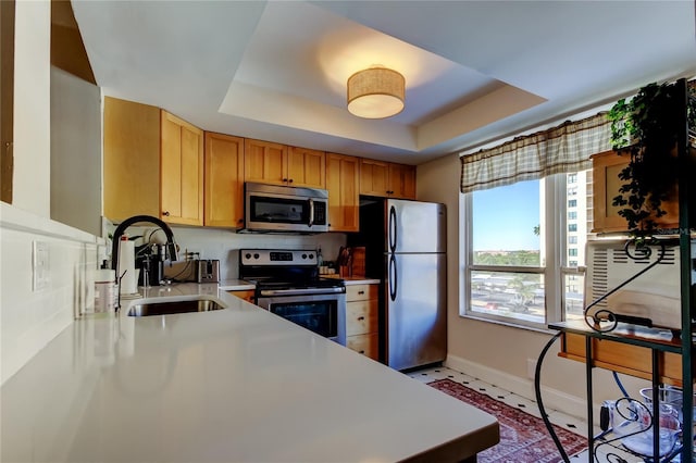 kitchen featuring stainless steel appliances, a sink, a tray ceiling, baseboards, and light countertops