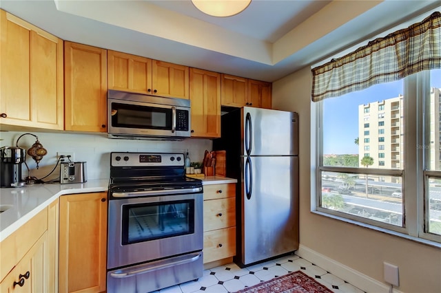 kitchen with appliances with stainless steel finishes, light flooring, light countertops, baseboards, and a tray ceiling