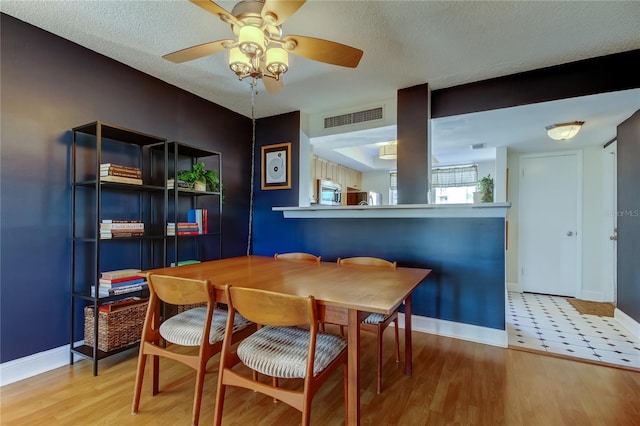 dining area featuring baseboards, wood finished floors, a ceiling fan, and a textured ceiling