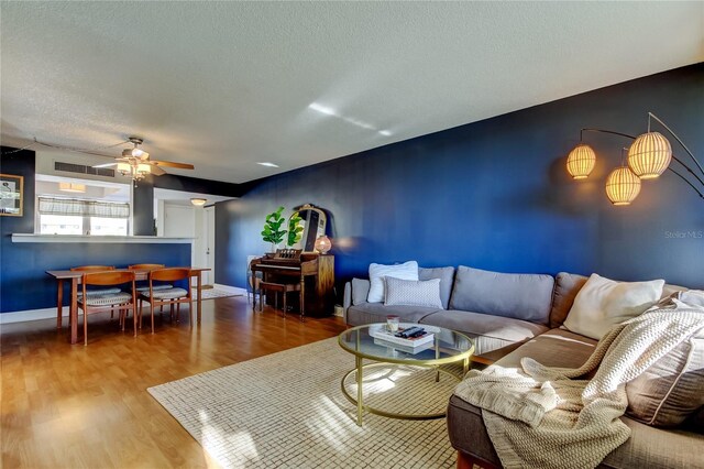 living room with wood finished floors, a ceiling fan, a textured ceiling, and baseboards