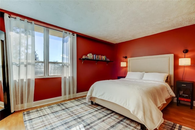 bedroom with wood finished floors, baseboards, and a textured ceiling
