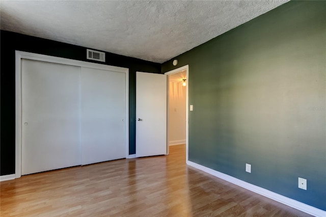 unfurnished bedroom with light wood finished floors, a textured ceiling, a closet, and baseboards