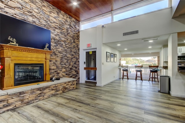 living room featuring wood finished floors, baseboards, a high ceiling, and a stone fireplace