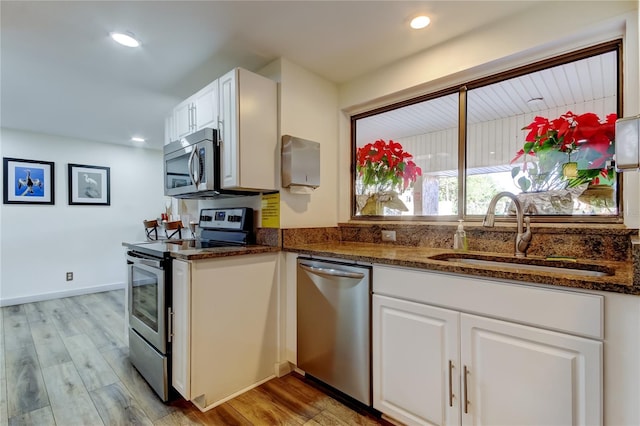 kitchen featuring appliances with stainless steel finishes, a sink, white cabinetry, dark stone countertops, and light wood-style flooring