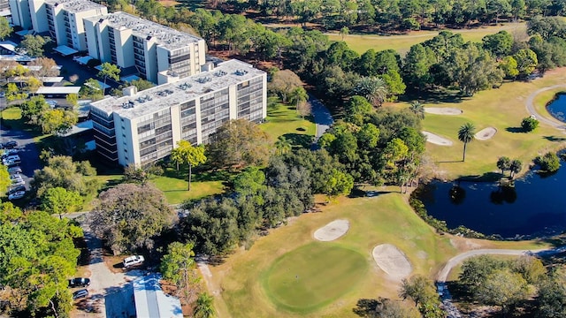 drone / aerial view of apartment complex / building, a large body of water, a golf course, and a tree filled landscape