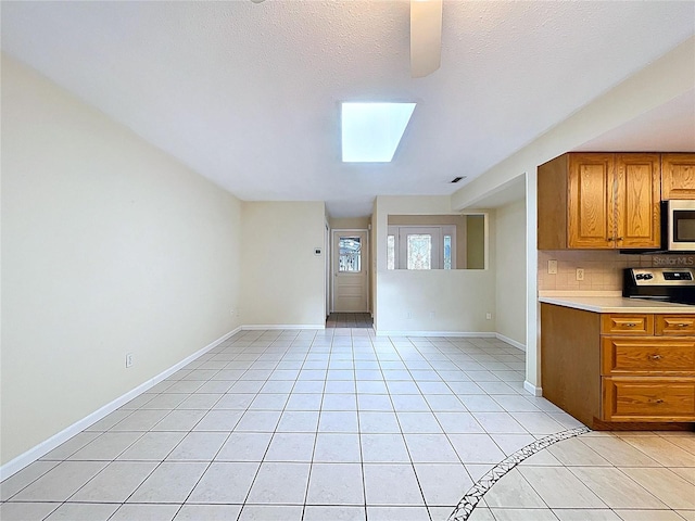 232 Pinecrest Dr, Palm Harbor, FL 34683 - kitchen with stainless steel microwave, brown cabinetry, backsplash, light countertops, and light tile patterned floors