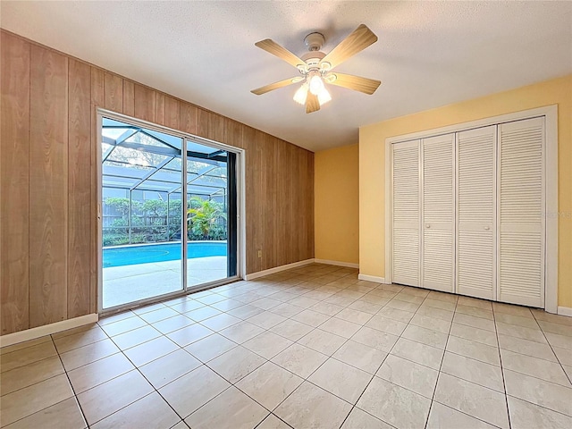 232 Pinecrest Dr, Palm Harbor, FL 34683 - unfurnished bedroom featuring access to exterior, wood walls, light tile patterned floors, ceiling fan, and a closet