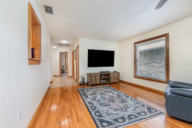 living area featuring baseboards, visible vents, a textured ceiling, and wood finished floors