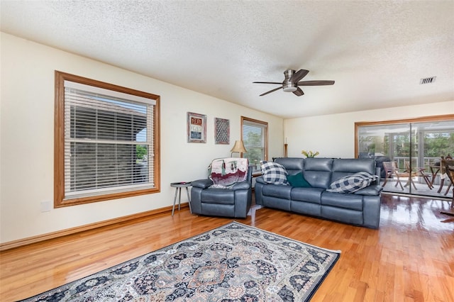living room featuring a textured ceiling, visible vents, wood finished floors, and ceiling fan