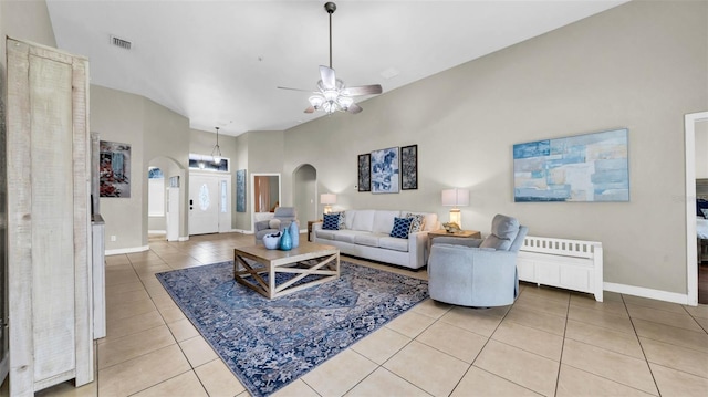 living room featuring arched walkways, tile patterned flooring, a ceiling fan, radiator heating unit, and baseboards