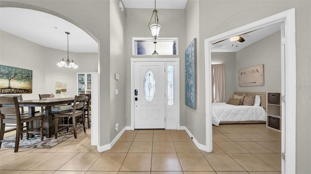 foyer featuring a towering ceiling, light tile patterned floors, baseboards, a chandelier, and arched walkways