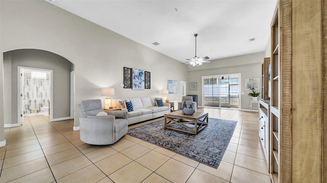 living area with arched walkways, light tile patterned floors, ceiling fan, and baseboards