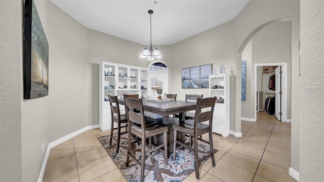 dining area featuring light tile patterned floors, arched walkways, baseboards, a chandelier, and a high ceiling