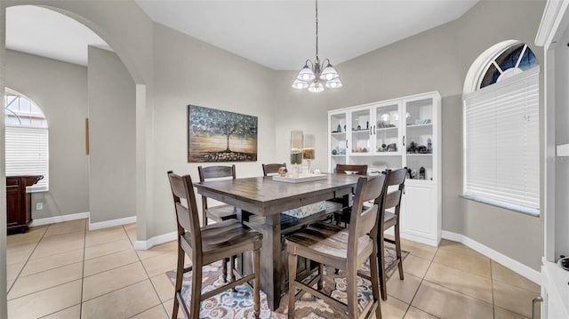 dining space with light tile patterned floors, arched walkways, a chandelier, and baseboards