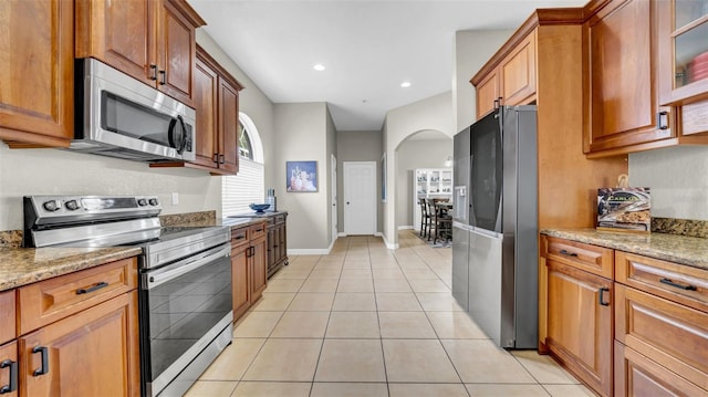 kitchen with appliances with stainless steel finishes, arched walkways, light stone countertops, light tile patterned floors, and recessed lighting