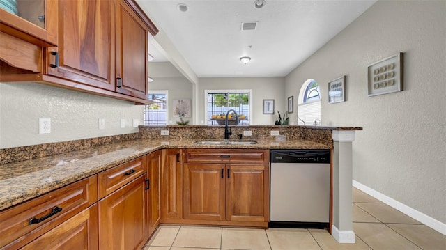 kitchen featuring stainless steel dishwasher, a sink, a peninsula, stone counters, and light tile patterned floors