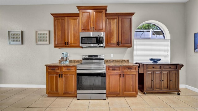 kitchen with appliances with stainless steel finishes, light stone countertops, brown cabinets, baseboards, and light tile patterned floors