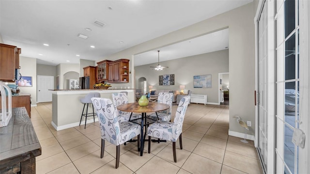 dining area featuring light tile patterned floors, ceiling fan, baseboards, arched walkways, and radiator