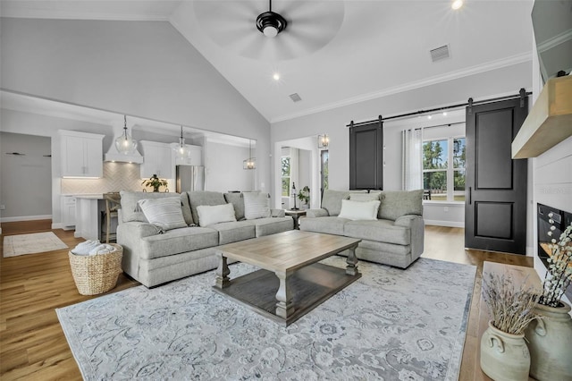 14902 Sweat Loop Rd, Wimauma, FL 33598 - living room featuring light wood-style flooring, a barn door, high vaulted ceiling, ceiling fan, and ornamental molding