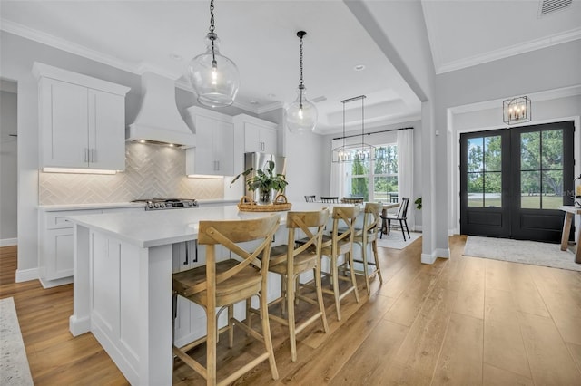 14902 Sweat Loop Rd, Wimauma, FL 33598 - kitchen with premium range hood, light countertops, a spacious island, light wood-style floors, and white cabinetry