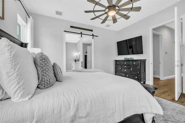 14902 Sweat Loop Rd, Wimauma, FL 33598 - bedroom with a barn door, wood finished floors, a ceiling fan, baseboards, and connected bathroom
