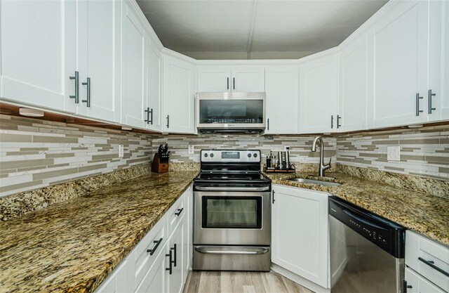1290 Pine Ridge Cir E Unit G1, Tarpon Springs, FL 34688 - kitchen with appliances with stainless steel finishes, a sink, dark stone counters, decorative backsplash, and white cabinets