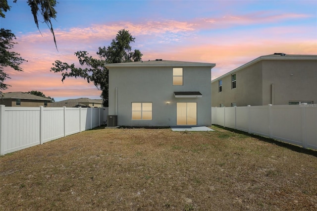 back of property at dusk featuring central air condition unit, stucco siding, a lawn, and a fenced backyard