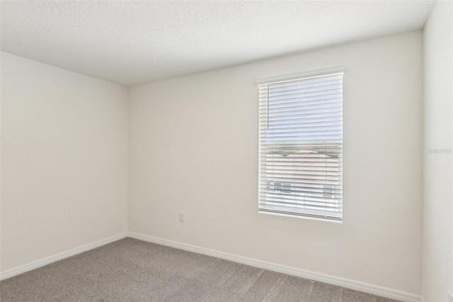 spare room featuring light colored carpet, a textured ceiling, and baseboards