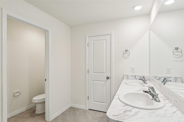 bathroom with toilet, baseboards, double vanity, and a sink