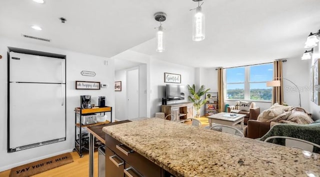 kitchen with freestanding refrigerator, light stone counters, visible vents, open floor plan, and light wood-style floors