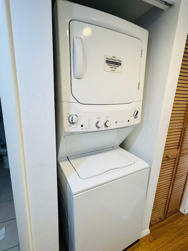clothes washing area with laundry area, stacked washer and dryer, and wood finished floors