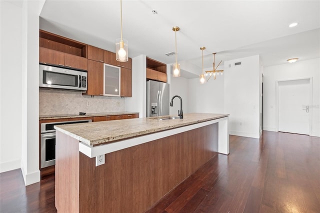 kitchen featuring stainless steel appliances, light countertops, a kitchen island with sink, decorative backsplash, and dark wood-style floors