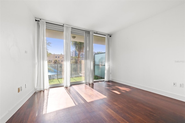 empty room featuring wood finished floors, baseboards, and expansive windows