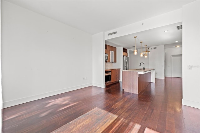 unfurnished living room with dark wood finished floors, a sink, baseboards, a chandelier, and recessed lighting