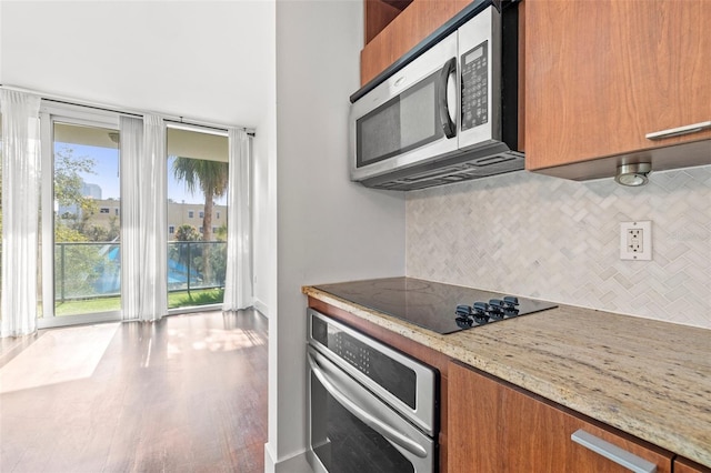 kitchen with stainless steel appliances, brown cabinetry, decorative backsplash, light stone countertops, and wood finished floors