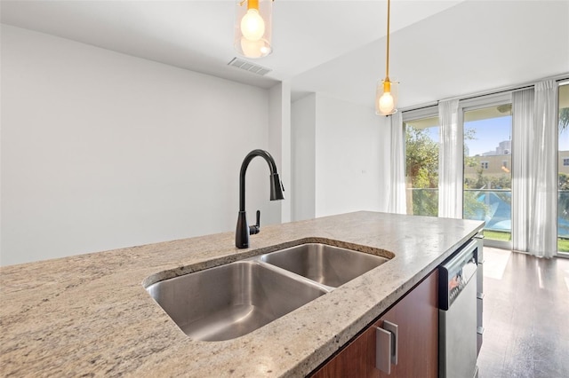 kitchen featuring dishwasher, a sink, light stone countertops, decorative light fixtures, and wood finished floors
