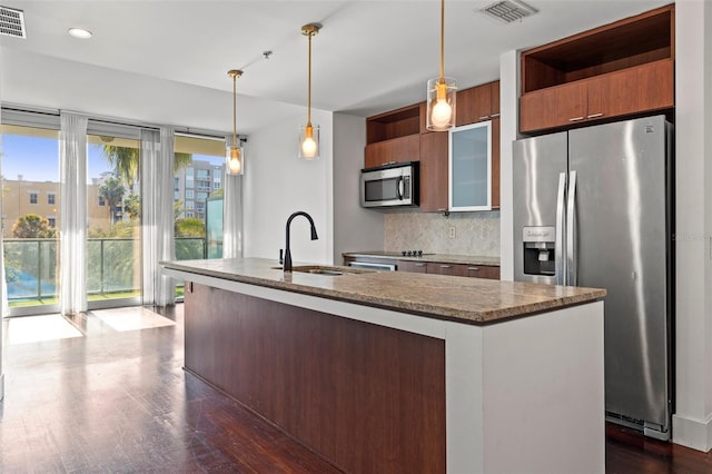 kitchen featuring appliances with stainless steel finishes, a sink, an island with sink, tasteful backsplash, and dark wood finished floors