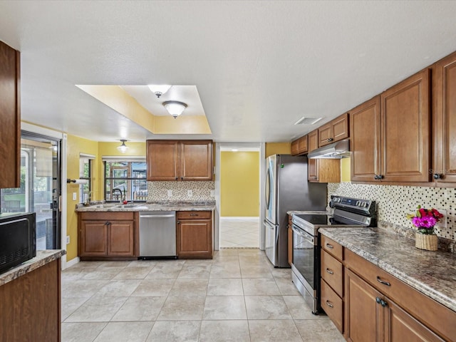kitchen with under cabinet range hood, brown cabinets, decorative backsplash, and appliances with stainless steel finishes