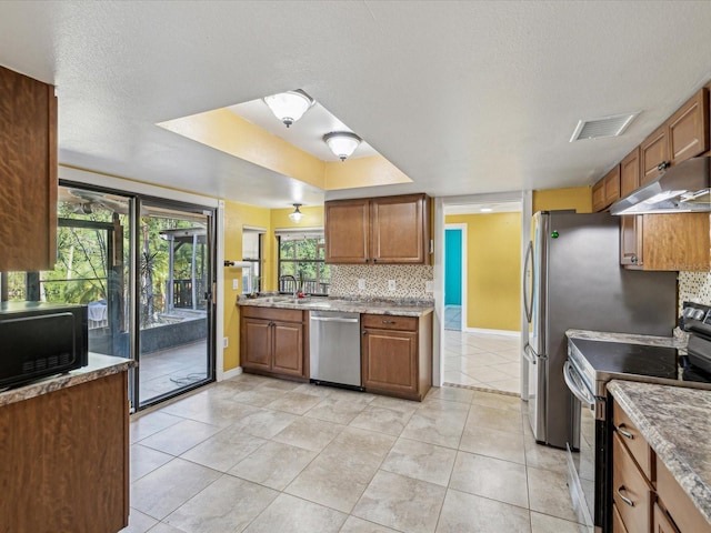 kitchen with a sink, stainless steel appliances, under cabinet range hood, backsplash, and baseboards