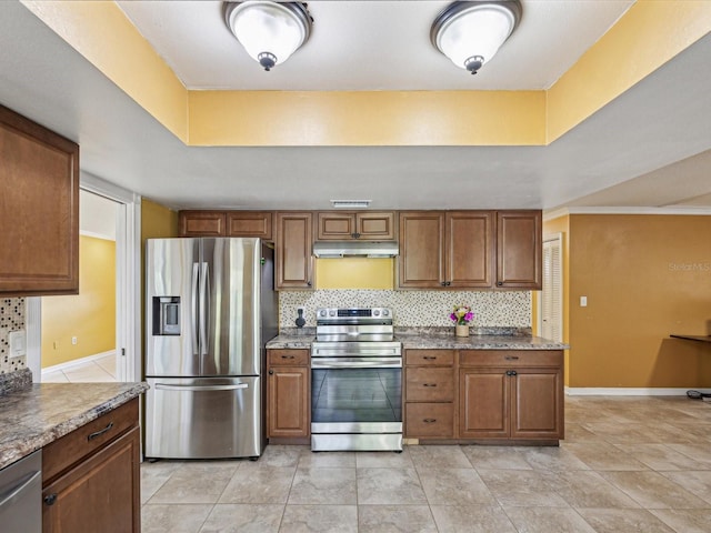 kitchen featuring under cabinet range hood, stainless steel appliances, tasteful backsplash, and brown cabinetry