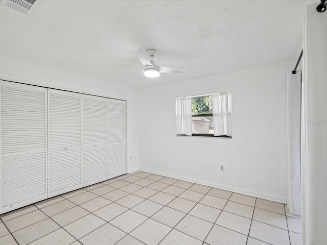 unfurnished bedroom with light tile patterned floors, a ceiling fan, a closet, a textured ceiling, and visible vents