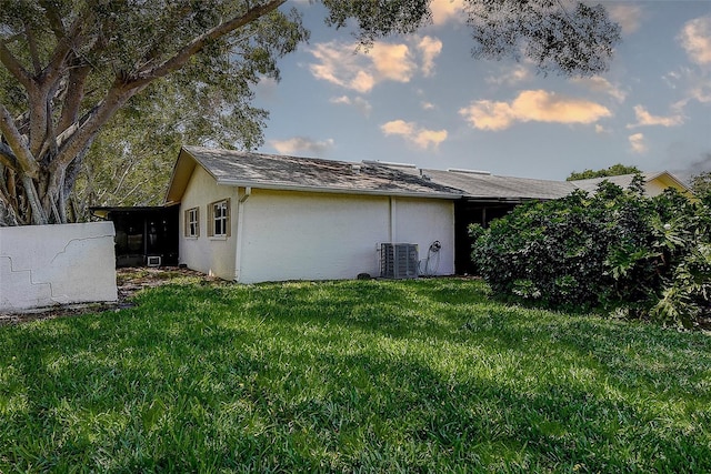 rear view of property with central AC, a sunroom, a lawn, and stucco siding